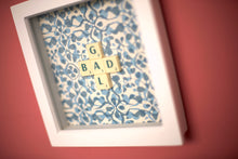 Load image into Gallery viewer, Characterful and colourful scrabble art blue patterned background with 'Donut' written in mixed coloured vintage scrabble tiles presented in a white box frame