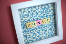 Load image into Gallery viewer, Characterful and colourful scrabble art blue patterned background with 'Donut' written in mixed coloured vintage scrabble tiles presented in a white box frame