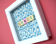 Load image into Gallery viewer, Characterful and colourful scrabble art blue patterned background with 'Donut' written in mixed coloured vintage scrabble tiles presented in a white box frame