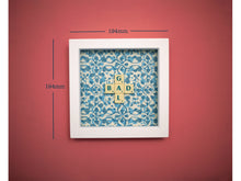 Load image into Gallery viewer, Characterful and colourful scrabble art blue patterned background with &#39;Donut&#39; written in mixed coloured vintage scrabble tiles presented in a white box frame 
