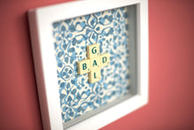 Load image into Gallery viewer, Characterful and colourful scrabble art blue patterned background with &#39;Donut&#39; written in mixed coloured vintage scrabble tiles presented in a white box frame 
