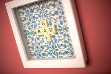 Load image into Gallery viewer, Characterful and colourful scrabble art blue patterned background with &#39;Donut&#39; written in mixed coloured vintage scrabble tiles presented in a white box frame 
