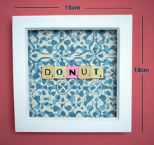 Load image into Gallery viewer, Characterful and colourful scrabble art blue patterned background with &#39;Donut&#39; written in mixed coloured vintage scrabble tiles presented in a white box frame 
