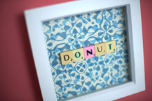 Load image into Gallery viewer, Characterful and colourful scrabble art blue patterned background with &#39;Donut&#39; written in mixed coloured vintage scrabble tiles presented in a white box frame 
